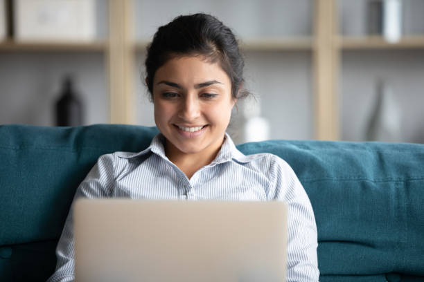 istock Indian girl using laptop seated on comfy couch at home 1311475103