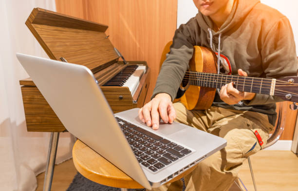 man enjoy playing guitar and learning music lesson online from internet in living room. e-learning concept
