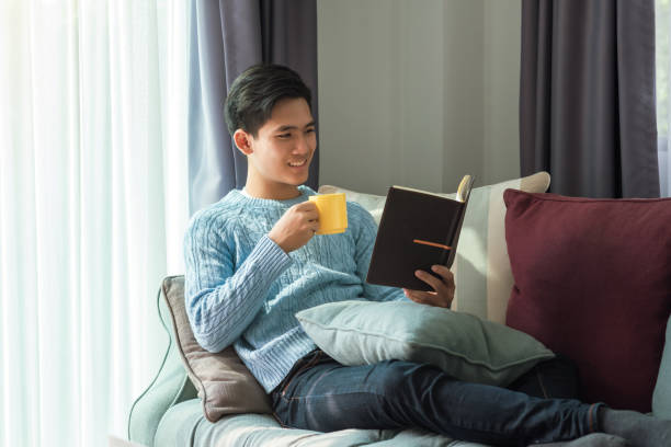 istock Happy young man on holiday drinking coffee, reading book at home on the sofa. 1311484980