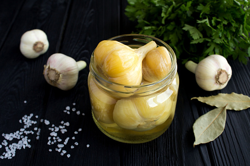 Pickled garlic in the glass jar on the black wooden background. Homemade fermented product. Close-up.