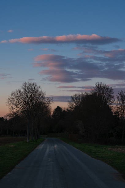 istock A country road in the dark under clouds lit by the setting sun. 1311491317