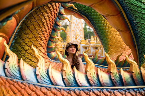 Happy young asian woman smiling in colorful serpent statue at Wat Phra That Nong Bua temple, Ubon Ratchathani
