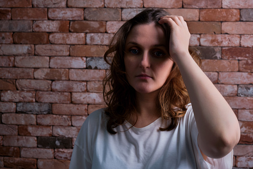 Portrait of an adult woman with problems in dramatic light against a red brick wall