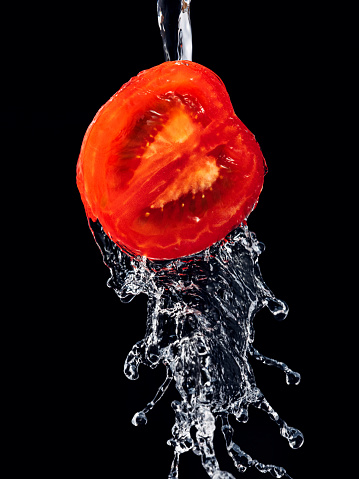 A broad stream of water flows from the tomato on a black background