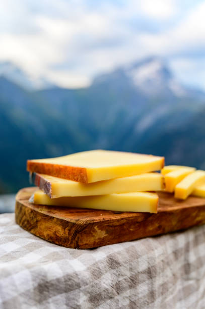 Cheese collection, French comte, beaufort or abondance cow milk cheese served outdoor with Alps mountains peaks on background Cheese collection, French comte, beaufort or abondance cow milk cheese served outdoor with Alps mountains peaks in summer on background jura france stock pictures, royalty-free photos & images