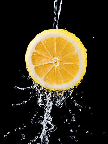 slice of lemon entering and splashing into a glass of water, fruit, black background, concept of vitality, health, well being