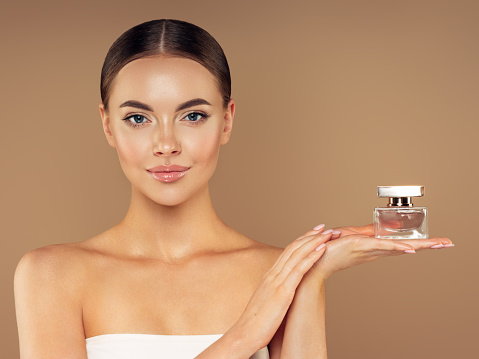 Young woman with clean and fresh skin presenting perfume