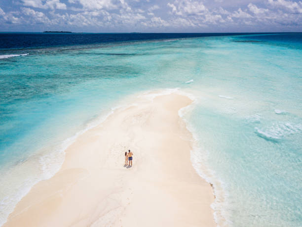 Young adult couple standing on a sandbank against turquoise water in Maldives Young adult couple standing on a sandbank against turquoise water in Maldives sandbar stock pictures, royalty-free photos & images