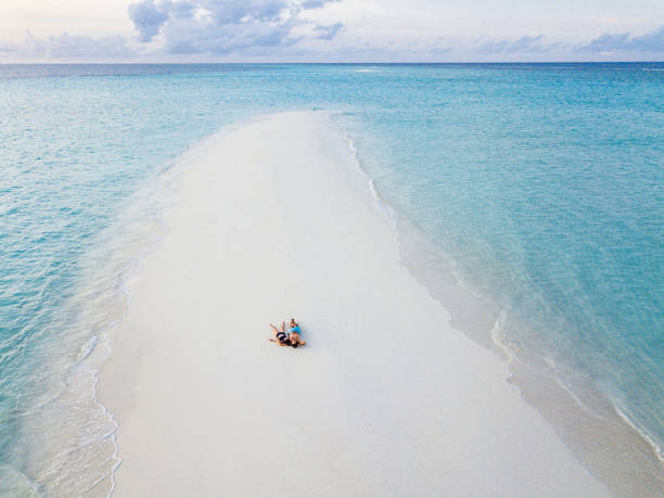 junges erwachsenes paar liegt zusammen auf einer sandbank gegen türkisfarbenes wasser auf den malediven - beach men isolated tourist stock-fotos und bilder