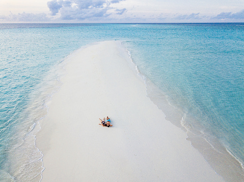 Young adult couple lying together on a sandbank against turquoise water in Maldives
