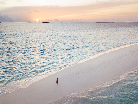 Young adult woman standing on a sandbank against turquoise water in Maldives at sunset