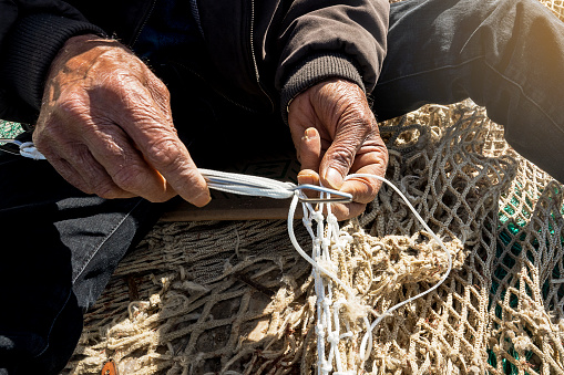 old fisherman hand sews a fishing net on the pier. lost traditional work