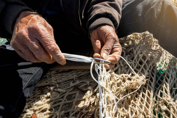 old fisherman sews a fishing net whit his wringle hand stock photo