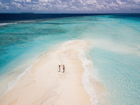 Young adult couple standing on a sandbank against turquoise water in Maldives