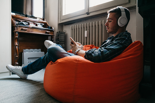 Young adult man texting and listening to music in his bedroom