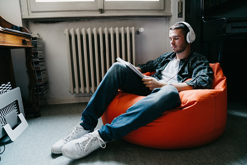 Young adult man reading and listening to music in his bedroom