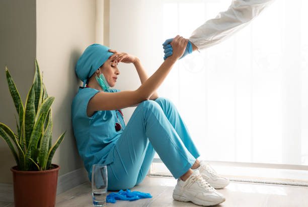 le professionnel médical féminin surchargé porte le masque facial, l’uniforme bleu et les gants se repose sur le plancher d’hôpital - mental health professional photos et images de collection