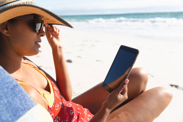istock Mixed race woman on beach holiday sitting in deckchair using tablet 1311501897