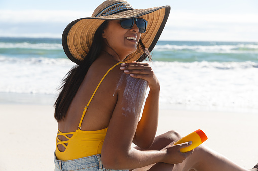 Mujer de raza mixta sonriente en vacaciones en la playa usando crema para protector solar photo