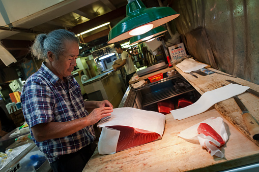 Horizontal view of a Japanese fishmonger wrapping a piece of red tuna with paper in the Seafood Intermediate Wholesalers' Area interior, Tsukiji Market, Tsukiji district, Tokyo