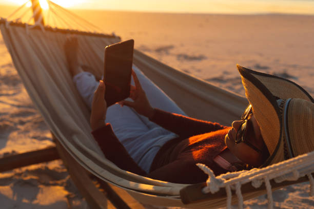 istock Mixed race woman on beach holiday lying in hammock using tablet during sunset 1311504920