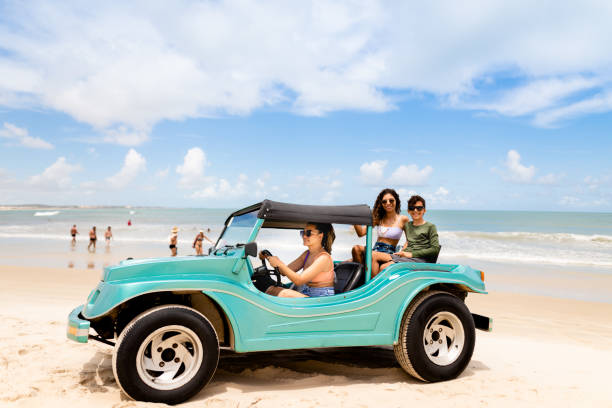 Mom driving her two smiling children in a beach buggy by the ocean in the summer