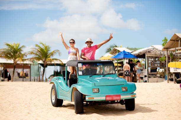 uśmiechnięta para stojąca z tyłu buggy na plaży i macha - beach buggy zdjęcia i obrazy z banku zdjęć