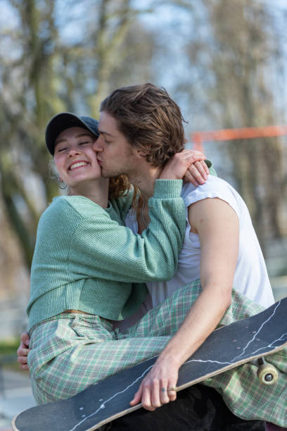 junge mit skateboard küssen mädchen auf der wange - 20s berlin germany heterosexual couple boyfriend stock-fotos und bilder