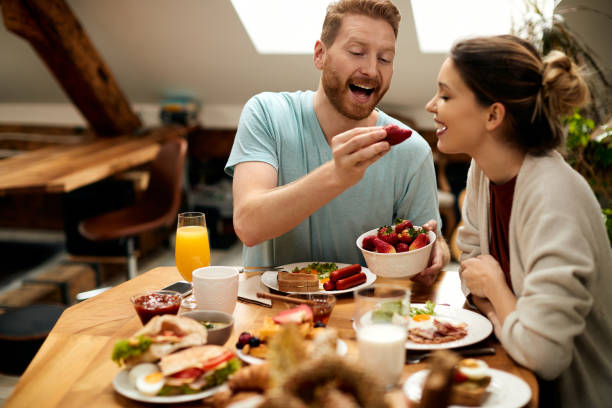 istock Happy man feeding his girlfriend with strawberries during breakfast at dining table. 1311512559
