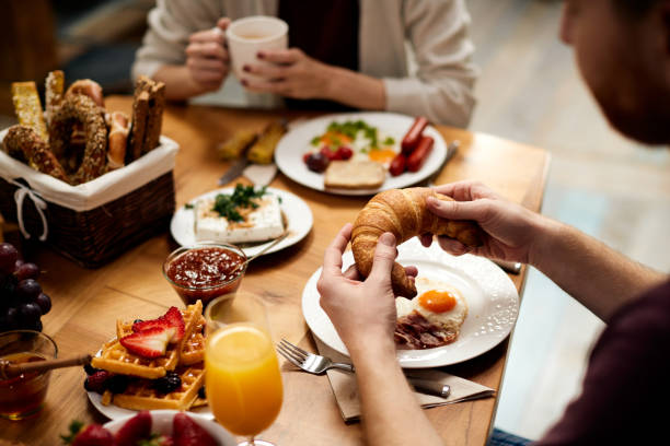 istock Close-up of man eating croissant while having breakfast with his girlfriend at dining table. 1311512743