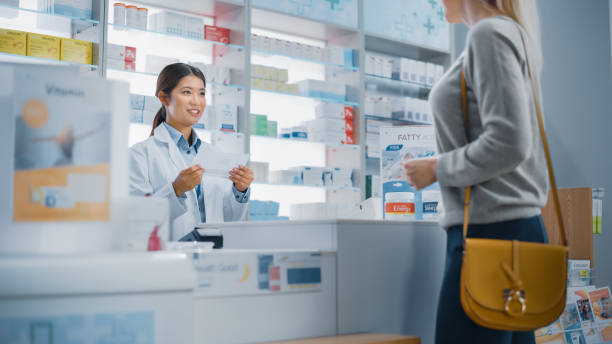 Pharmacy Drugstore Checkout Counter: Customer gives Prescription to Professional Female Pharmacist who Finds Medicine Package, Explains how to Use it. Pharmacy Drugstore Checkout Counter: Customer gives Prescription to Professional Female Pharmacist who Finds Medicine Package, Explains how to Use it. asian cashier stock pictures, royalty-free photos & images