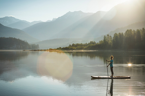 Woman paddleboarding on calm lake in Whistler during sunrise.