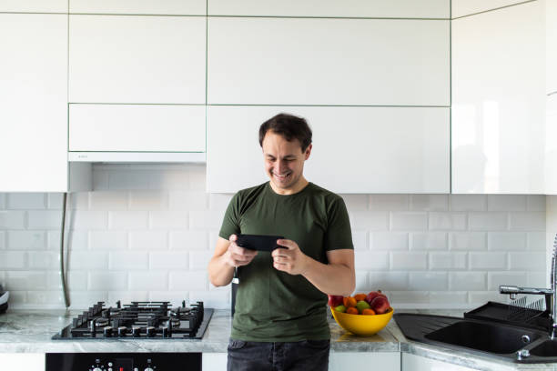 istock Smiling young man use cellphone gadget texting messaging while preparing food in kitchen. Happy millennial male read recipe on smartphone get ready for home party or celebration 1311516572