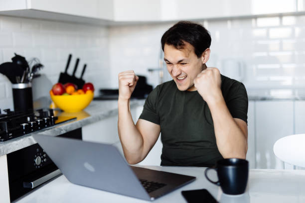 istock Excited man sit at table in kitchen feel euphoric win online lottery on laptop. Overjoyed young male in spectacles look at computer screen triumph get good news on email 1311516588