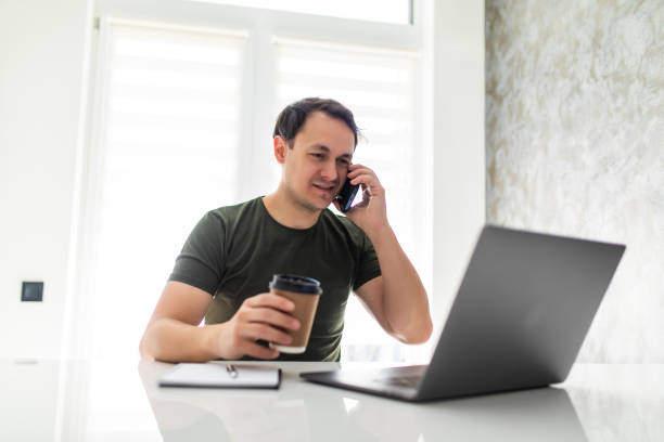 istock Young handsome man working from home in the kitchen with a laptop talking on mobile 1311516676
