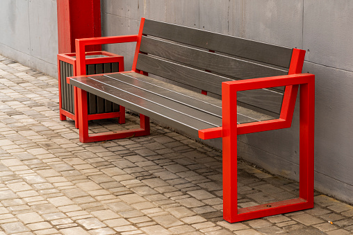 street wooden seat with red metal railing and a garbage can