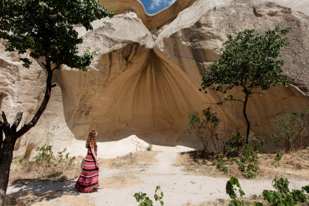 Young woman walking among rocks in Capadocia, wearing a red dress. The trees around it.