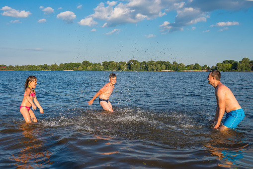 Family games in the water on a sunny day. Father with children playing in the river. Vacation, vacation, active lifestyle.