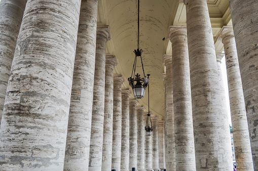 Vatican - May 11, 2018: Medieval colonnade of St. Peter's Basilica on St. Peter's square with lamps hanging from top in Vatican, center of Rome, Italy
