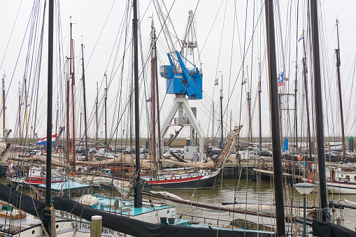 View on the harbor of Harlingen in The Netherlands with a maze of masts from traditional sailing ships. In the background the Harbor Crane Hotel.