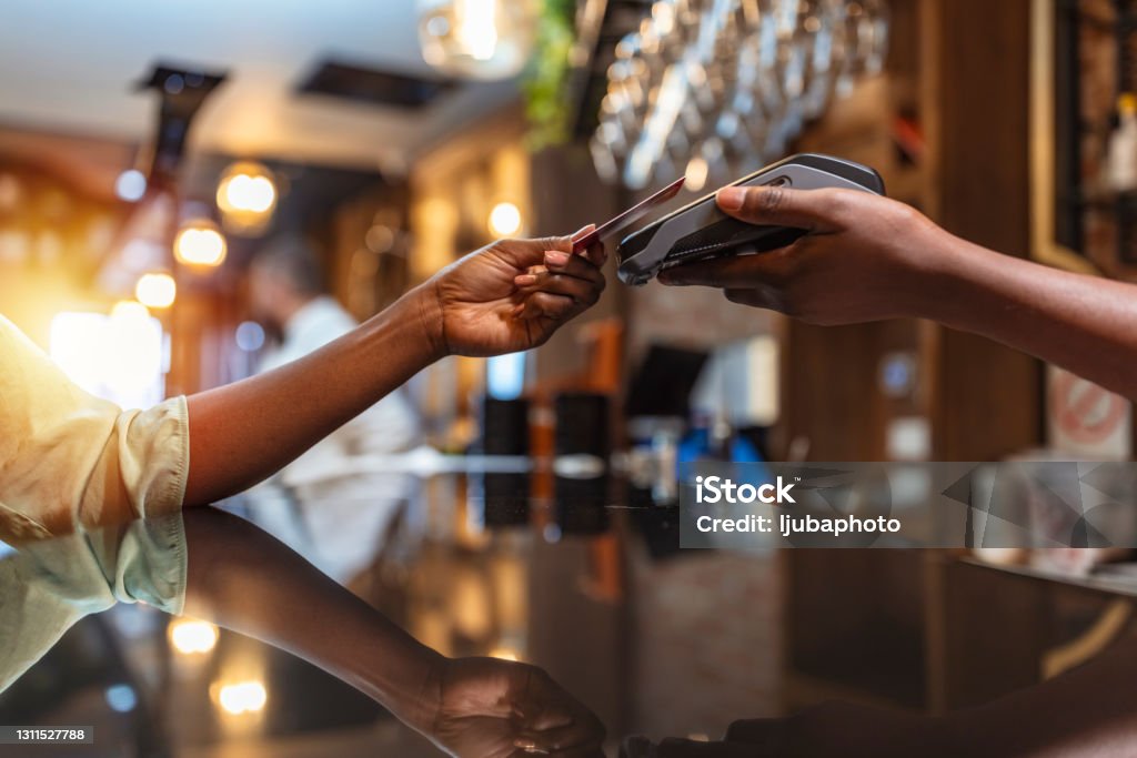 Woman paying with mobile phone at bar NFC Technology. Close up of black female, giving credit card to waiter paying with red credit card in café Paying Stock Photo