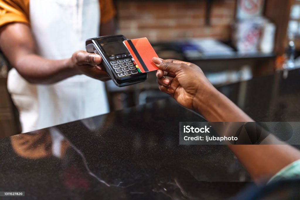Cropped shot of an unrecognizable woman paying for her purchase by card NFC Technology. Close up of black female, giving credit card to waiter paying with red credit card in café Paying Stock Photo