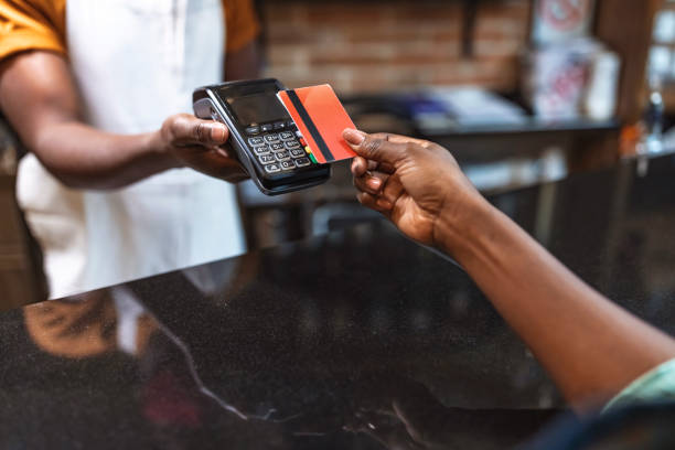 Cropped shot of an unrecognizable woman paying for her purchase by card NFC Technology. Close up of black female, giving credit card to waiter paying with red credit card in café credit card purchase stock pictures, royalty-free photos & images