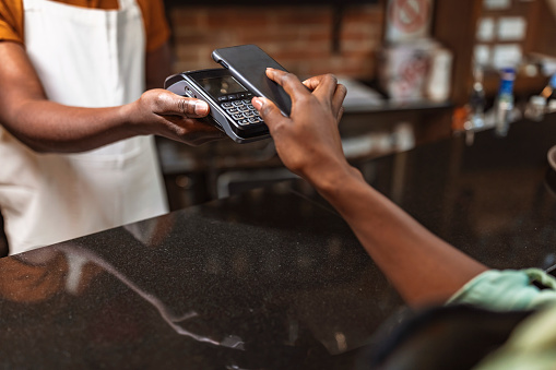 Shot of a barista taking a smartphone payment from a customer at a café