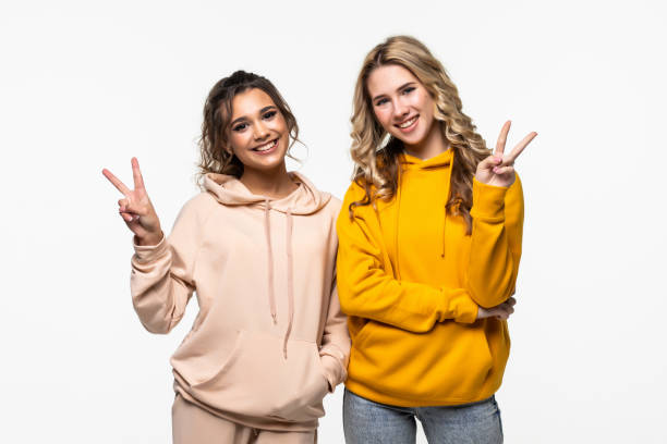istock Two happy women posing together and showing peace gestures while looking at the camera over white background 1311529573