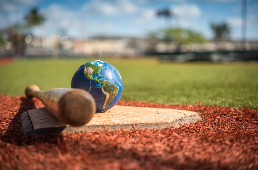 Planet Earth with baseball bat, glove and ball on synthetic ground. The globalization of baseball increases the quality of this American pastime and its famous world series. Visual references from NASA (https://visibleearth.nasa.gov/images/74117/august-blue-marble-next-generation).