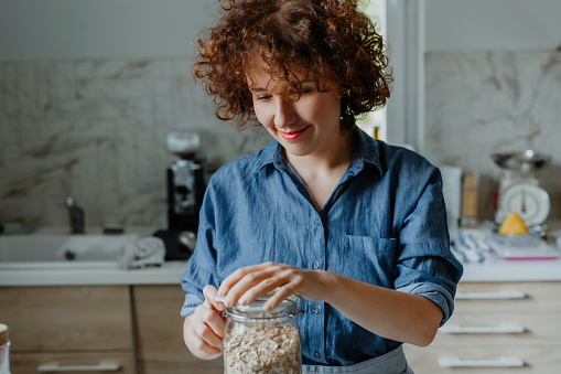 Beautiful Caucasian woman smiling and making breakfast with rolled oats in the kitchen