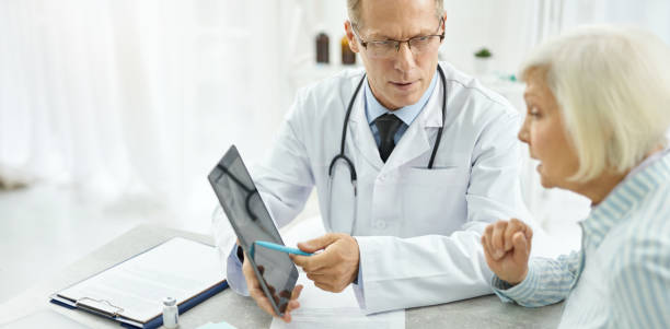 istock Male doctor using tablet computer and talking with patient in clinic 1311536006