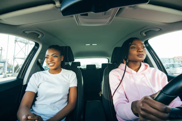 istock Two attractive young african girlfriends talking and laughing together while driving in a car through the city on a sunny day. 1311536833