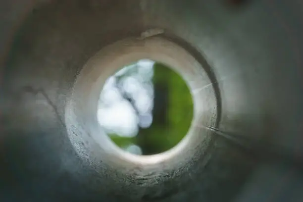 Photo of looking into a metal pipe with blur green tree at the end